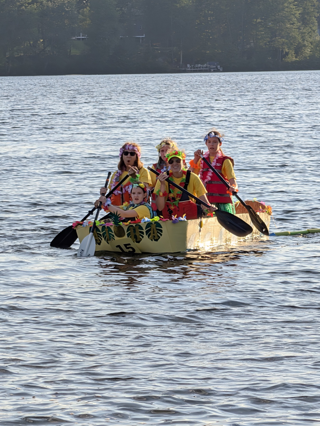 The Unsinkable Luau crew paddling the yellow cardboard boat across Lake Nipmuc